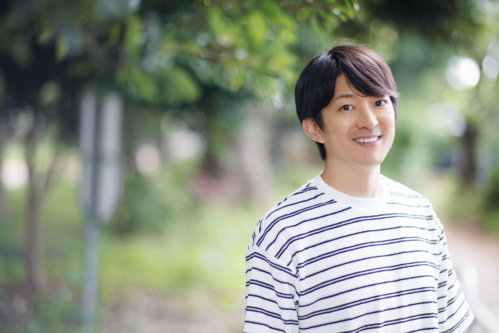 緑の木々を背に、ボーダーシャツ姿で穏やかに微笑む澤田智洋