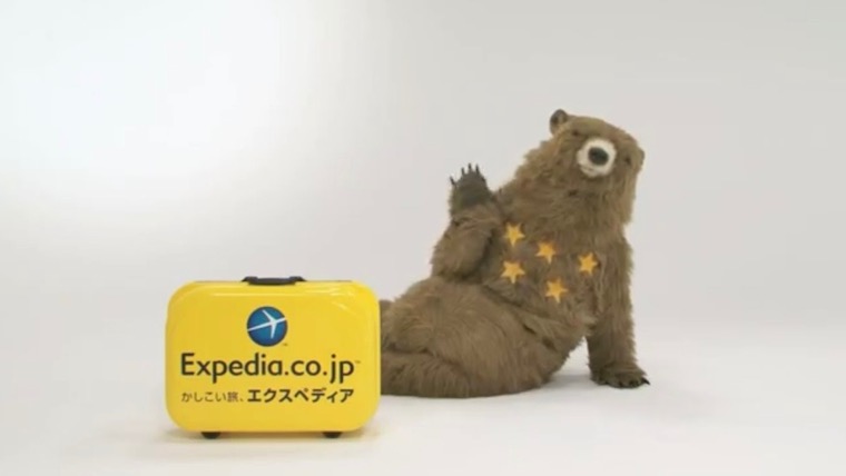 Expediaのくまのマスコットと黄色いスーツケース。「Expedia.co.jp／かしこい旅、エクスペディア」