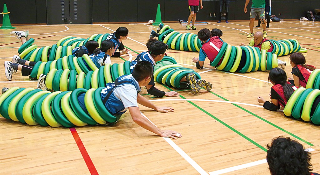 体育館でイモムシ型ウェアを着た選手たちが床を這いながらボールを追う試合風景