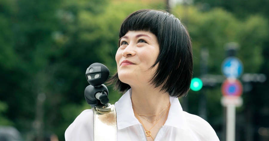 肩に視覚障害者アテンドロボットNIN_NINを乗せて空を見上げる女性